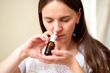 Young woman using nasal spray for relief from allergies or congestion, concept: at-home treatment