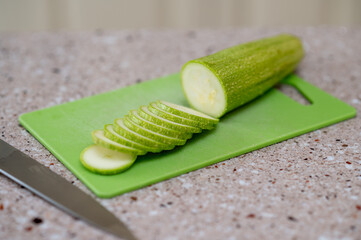 Fresh zucchini being sliced on a green cutting board in kitchen, concept: healthy cooking...