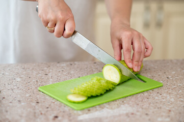 Close-up of hands slicing zucchini with a knife on a green board, concept: fresh meal preparation...