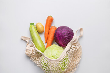Various healthy organic vegetables in natural textile eco-friendly wicker string bag on gray...