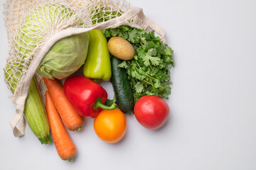 Various healthy organic vegetables in natural textile eco-friendly wicker string bag on gray background flat lay top view. Healthy food, seasonal products. Zero waste bag