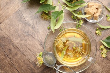 Fresh linden tea in cup, sugar cubes and flowers on wooden table, flat lay. Space for text