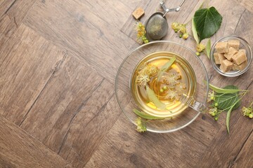 Fresh linden tea in cup, sugar cubes and flowers on wooden table, flat lay. Space for text