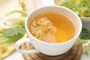Fresh linden tea in cup and flowers on white table, closeup