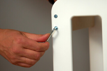 Hand tightening a screw on a white furniture piece during assembly at home