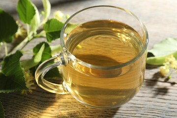 Fresh linden tea in cup and flowers on wooden table, closeup