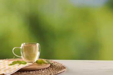 Tasty green tea in glass cup and leaves on white marble table outdoors, space for text