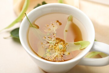 Fresh linden tea in cup and flowers on white table, closeup