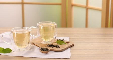 Tasty green tea in glass cups, brew and leaves on wooden table indoors, closeup. Space for text