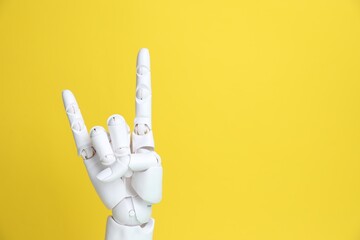 White mannequin hand making rock gesture on yellow background, space for text