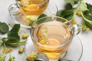 Fresh linden tea in cups and flowers on light grey table, closeup
