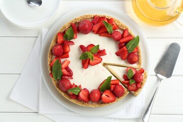 Delicious cheesecake with strawberries, mint, server and tea on white wooden table, flat lay