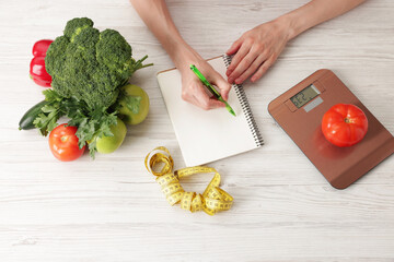 Woman developing diet plan at light wooden table with kitchen scale, measuring tape and healthy...