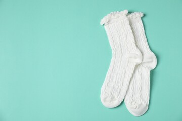 Pair of comfortable white socks on turquoise background, top view. Space for text