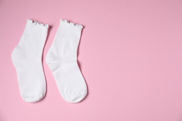 Pair of comfortable white socks on pink background, top view. Space for text