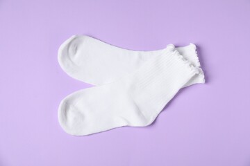 Pair of comfortable white socks on violet background, top view