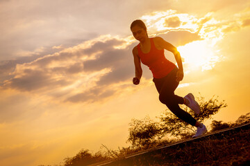 Silhouette of young woman running sprinting on road. Fit runner fitness runner during outdoor workout with sunset background