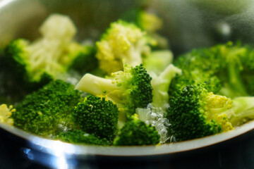 Cooking fresh broccoli in a saucepan over medium heat during a sunny afternoon