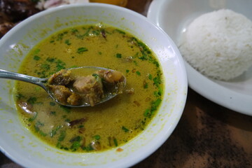Traditional Indonesian soto daging, a fragrant beef soup with herbs and spices, served with a side...