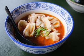 Traditional Chinese dumplings served in a blue-and-white bowl with hot chili broth and garnished with fresh green onions.