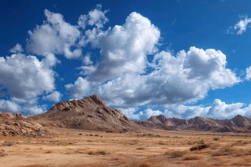 Fototapeta premium Vast arid landscape under a dramatic sky with puffy white clouds and rugged rocky outcrops