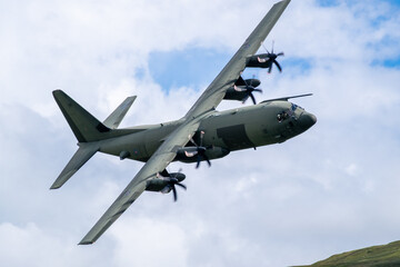 C-130 Hercules military transport aircraft is captured in flight from below, with its four...