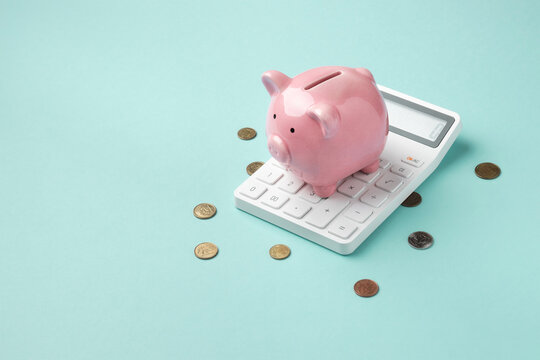A pink piggy bank rests on a calculator with scattered coins on a light turquoise background, symbolizing financial planning and savings calculation. High quality photo