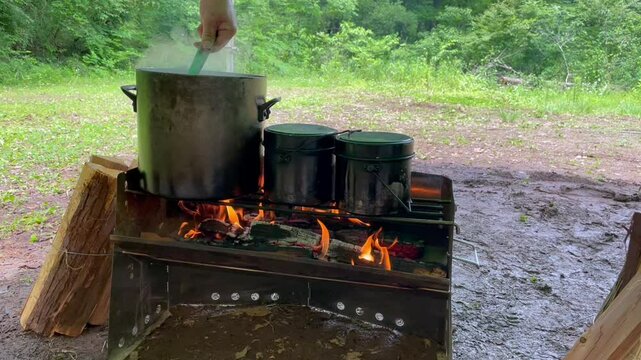 Cooking in a big pot and two small pots on an open fire with a fire stand. 