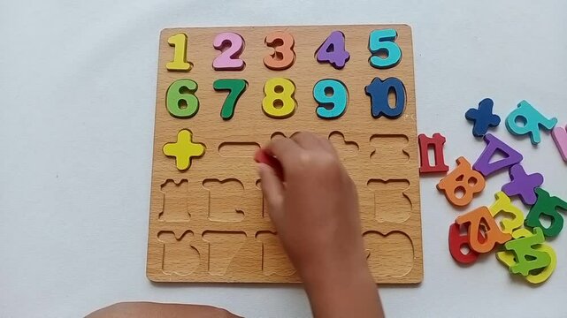 Asian child hand arranging colorful wooden number puzzle pieces on white background. Educational toy for learning counting and improving cognitive motor skills