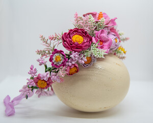 Handmade floral headband made of pink eva foam and pastic branches and stamens, displayed on ostrich egg, side view. Summer hair accessory for a girl.