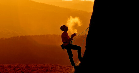A helmeted climber scaling a rock face at sunset, with a breathtaking mountain view in the background. A close-up shot highlights the climber's determination and focus.