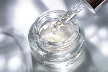Luxurious Skincare Serum Dropper and Jar on Reflective Surface.