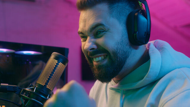 Excited winner champion Caucasian guy male gamer streamer man winning luck achievement victory internet win talking microphone play online game addict in headphones gaming streaming in neon dark room