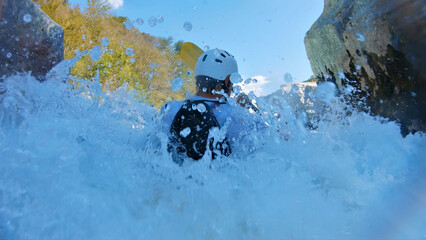 A thrilling kayaker, clad in a white helmet and blue jacket, navigates through turbulent waters...