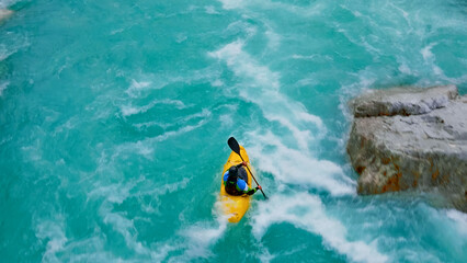 A thrilling aerial view captures a person kayaking in a yellow kayak, navigating through turbulent,...