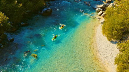 A breathtaking aerial view showcases two adventurers navigating their kayaks through a stunning, clear blue river surrounded by lush greenery. The kayakers skillfully maneuver their way around large.