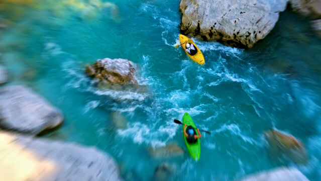 Two kayakers paddle through a narrow, rocky canyon surrounded by crystal-clear blue water. The aerial view showcases their thrilling journey as they navigate the rapids.