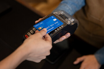 Close-up of blue credit card being inserted into POS terminal held by barista wearing brown apron...