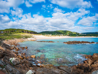 Clear day over Playa de Doniños Galicia Spain turquoise water rocky shore pine forest golden sand blue sky scattered clouds peaceful coastal village summer escape purity freedom