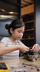 Fototapeta premium Asian girl student concentrates on assembling robotics project in classroom, showing science learning and focus.