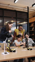 Asian girl student learning robotics with help from Caucasian and African female teachers, showing...