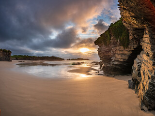 Sunset over Playa do Picón atlantic coast in Galicia Spain. Waves sandy shore golden light reflecting on water dramatic cliff peaceful atmosphere freedom escape solitude