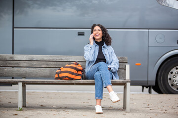 Happy travel woman sitting on a bench, chatting on her phone with a smile