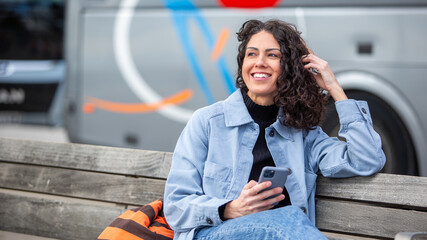 happy woman sitting on a bench smiling while holding a smartphone