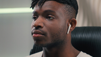 Close up happy smiling African American guy man ethnic male putting wireless headphones in ears...