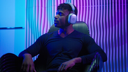 African American man guy male sitting in chair listening music in headphones using wireless...