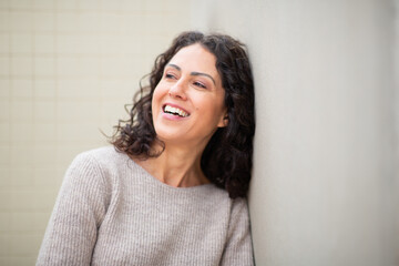 Portrait happy woman laughing while leaning against a wall