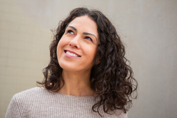 Confident middle-aged woman smiling gently while looking upward, standing outdoors in front of a...