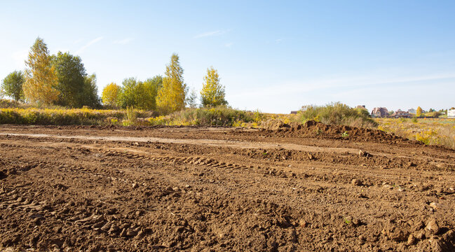 Empty land plot with tire prints prepared for new housing in rural area. Clearing and leveling of construction site. Earthworks for landscape design. Land reclamation for private property development.