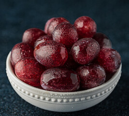 Close-up of wet red grapes in small white china bowl with dark background